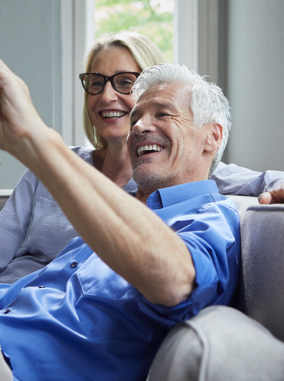 Happy mature couple sitting on couch at home taking a selfie